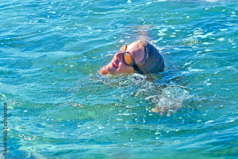 happy girl swims in swimming glasses on her back in the clear sea
