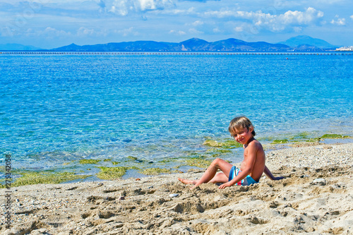 happy boy sitting on the golden sand near the sea