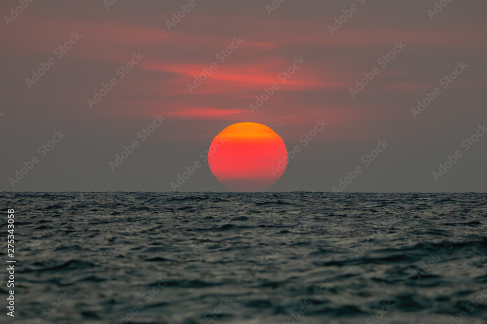 The sun is falling into the sea, the bottom of the sun eccentric because the refraction of the atmosphere. , The sky is orange And the sea is dark