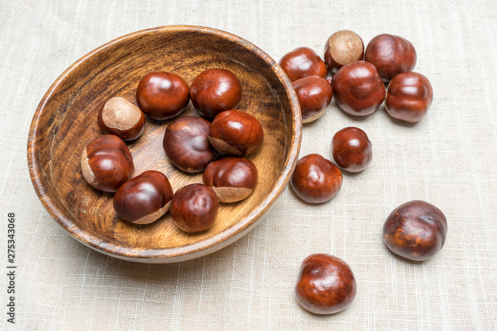 Fresh chestnut fruit scattered in wooden bowl and on light burlap fabric Fresh chestnut fruit scattered in wooden bowl and on light burlap fabric
