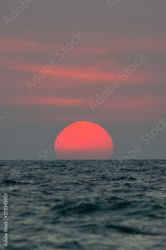 Fototapeta Naklejka Na Ścianę i Meble -  The sun fell to the sea, the bottom of the sun was blocked by the horizon. The sky is orange and the sea is dark.