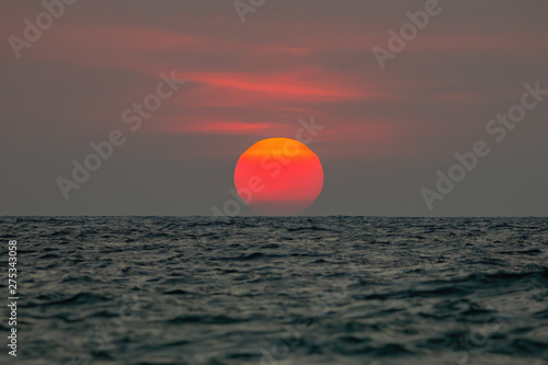 Fototapeta Naklejka Na Ścianę i Meble -  The sun is falling into the sea, the bottom of the sun eccentric because the refraction of the atmosphere. , The sky is orange And the sea is dark