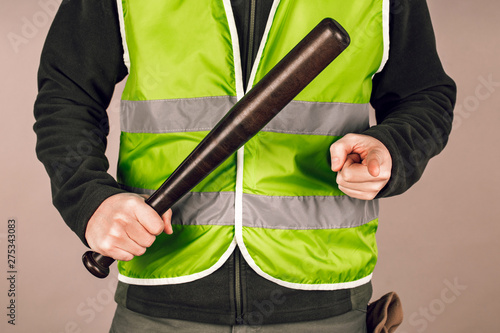 man in a yellow vest, a Builder or a protester with a baseball bat in his hands on a gray background