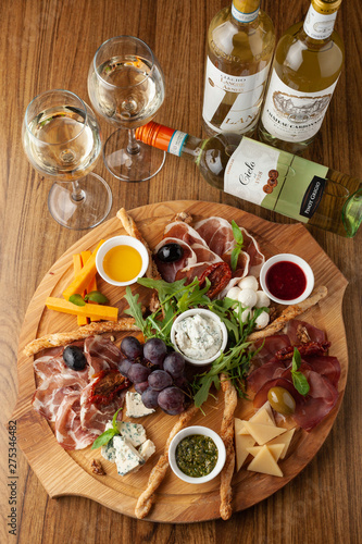 Classic antipasto with assortment of cold snacks to wine: cheddar cheese, blue cheese, prosciutto, chorizo, olives, rucola, olive oil and pesto, served on a wooden dish