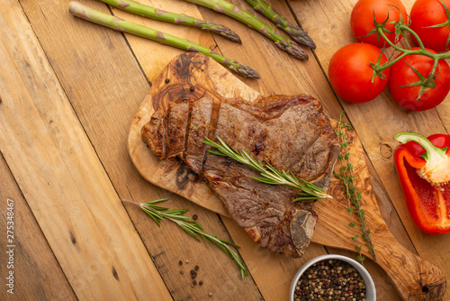 Marbled beef steak on a board with rosemary pepper, spices, and fresh vegetables, tomatoes and asparagus, artichoke, on a wooden background, restaurant menu, gastronomy, tasty food, restaurant service photo