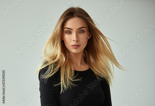 Slika na platnu Portrait of blonde woman with blowing hair looking at camera and isolated on gra