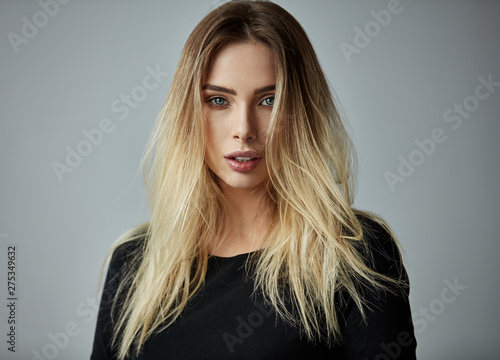 Blonde woman with long straight hair looking at camera isoalted on gray background