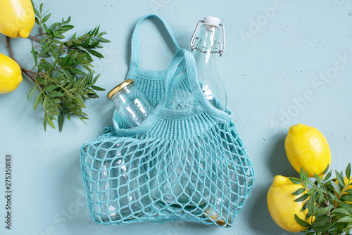 Blue background with mesh bag, glass bottle and jars decorated with fresh lemons