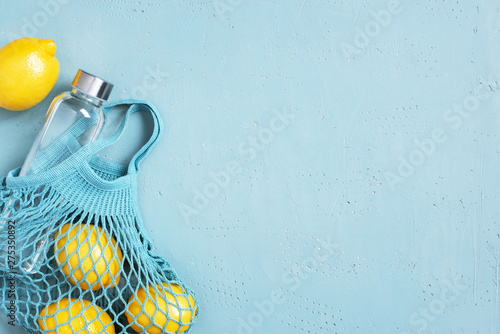 Blue background with mesh bag, glass bottle and fresh lemons