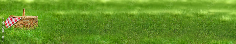 Fototapeta premium Wicker basket with blanket on green grass in park, space for text. Summer picnic