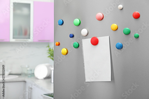 Empty sheet of paper with colorful magnets on refrigerator door in kitchen. Space for text