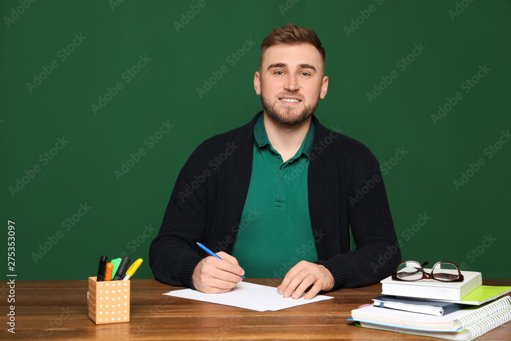 Portrait of young teacher at table against green background Portrait of young teacher at table against green background