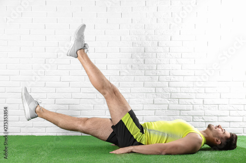 Handsome young man in sportswear doing scissors exercise on artificial green lawn near brick wall photo