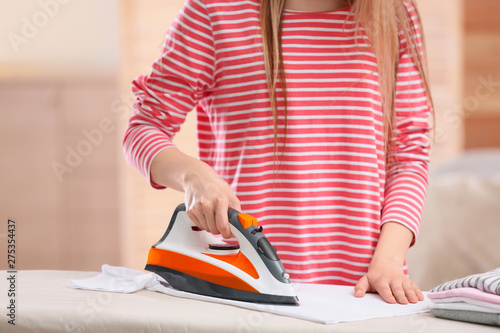 Young woman ironing clean laundry on board indoors, closeup