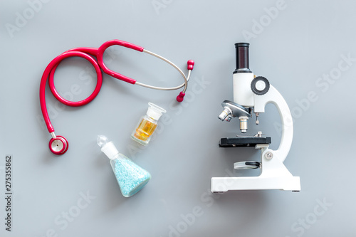 Medical tests on work table of doctor with microscope, stethoscope, test tube, pills on gray background top view