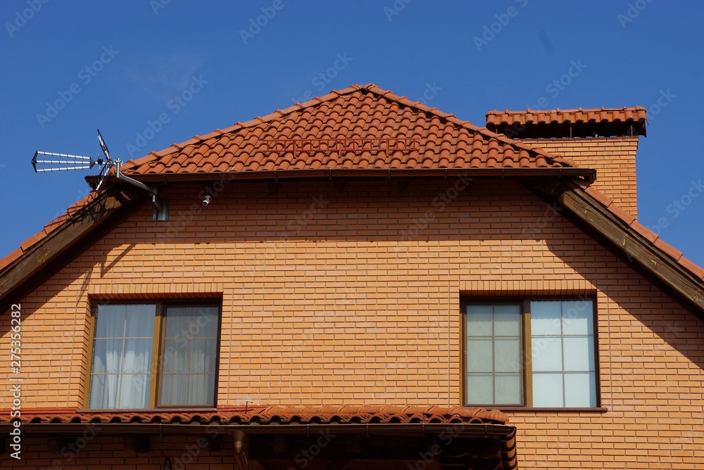 brown brick attic with windows under a tiled roof with a chimney against the blue sky brown brick attic with windows under a tiled roof with a chimney against the blue sky