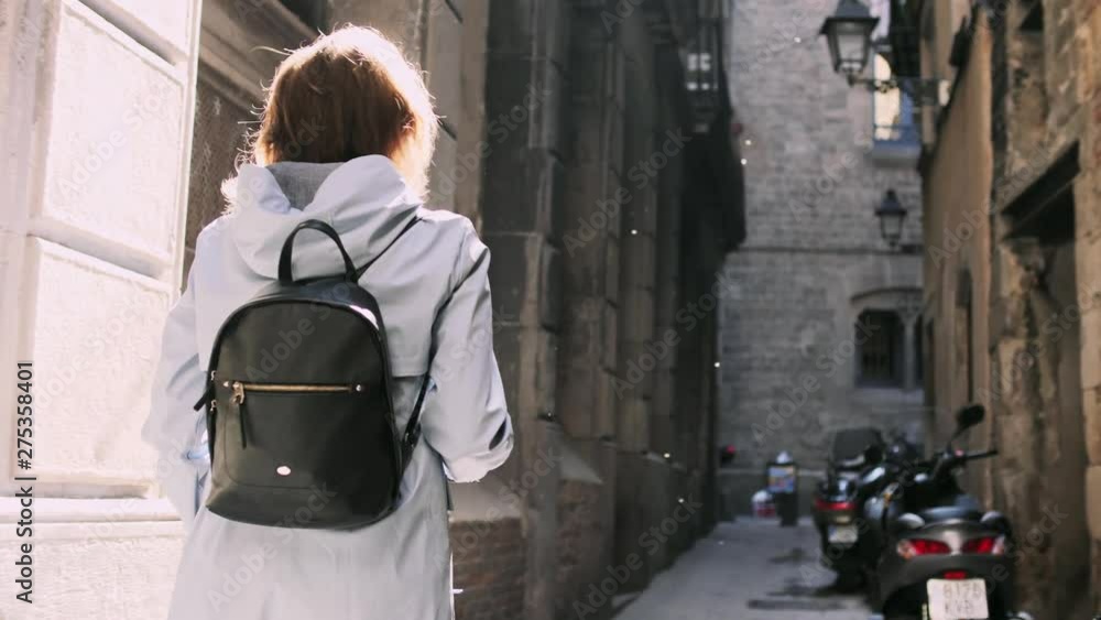 Back view of a girl with backpack walking through tight street. Stock ...