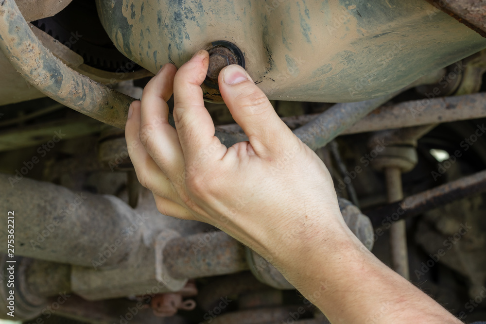Mechanic hand unscrews the cover of the engine crankcase to drain the waste oil.