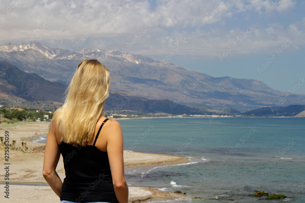 Blond woman looking down the coastline of Crete