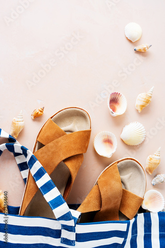 Striped beach bag with casual trendy leather sandals with crisscross details, shells on pink pastel background.  Vacation holidays layout. © PINKASEVICH