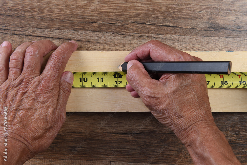 High angle closeup of a carpenters hands using a tape measure to mark a cut line on a board - obrazy, fototapety, plakaty 