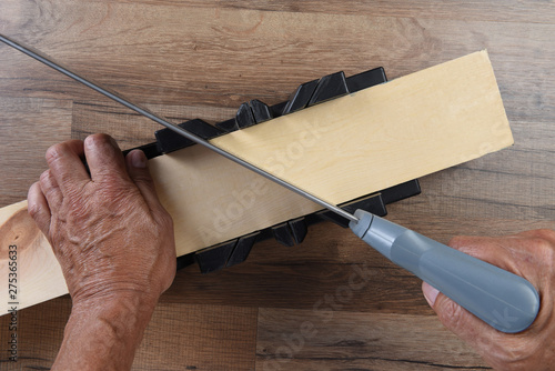 High angle closeup of a woodworker using a miter box and hand saw to cut a board at an angle photo