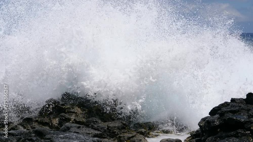 CLOSE UP: Large swell splashing over black volcanic rocks covering the rugged shore of Easter Island. Big blue waves coming from the Pacific approach the exotic island and crash into the rocky coast.