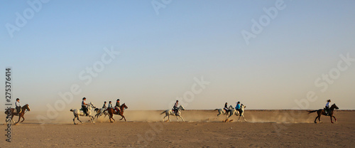 A group of people racing across the desert on Arabian horses. 