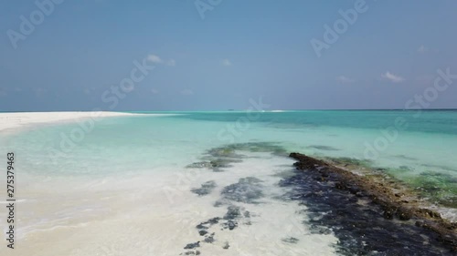 Camera moving from a white sand beach to some rocks in the shallow turquoise waters of Barbados photo