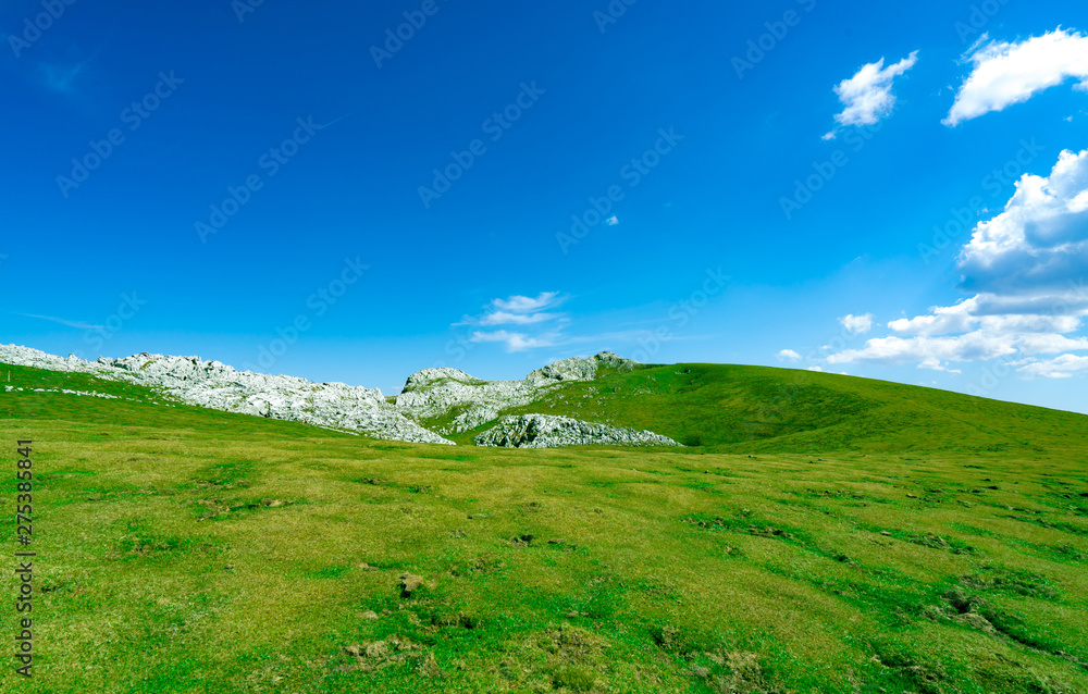 Landscape of green grass and rock hill in spring with beautiful blue sky and white clouds. Countryside or rural view. Nature background in sunny day. Fresh air environment. Stone on the mountain.