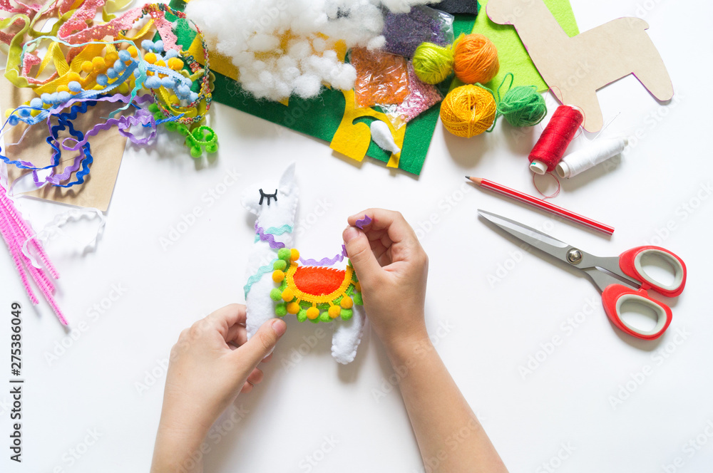 The hands of the child diy do handicraft toy lama. Felt soft craftsmanship.