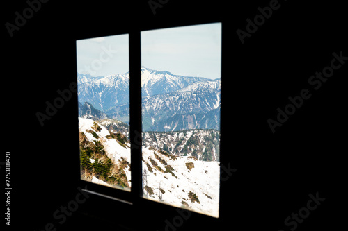 The ice-covered mountains in the late winter are seen from the window in a dark room.