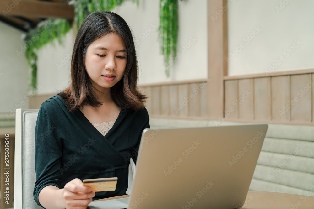 Closeup Asian beautiful woman Wearing a black shirt Sitting in the house Have a credit card in hand Is buying online products with a laptop computer Closeup Asian beautiful woman Wearing a black shirt Sitting in the house Have a credit card in hand Is buying online products with a laptop computer
