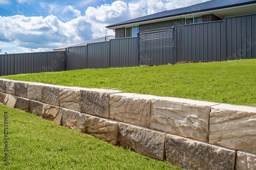 Stone retaining wall backyard green grass fence neighbour