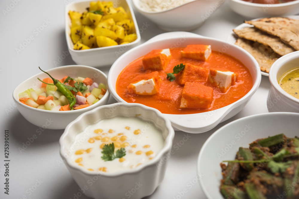 Assorted Indian food like paneer butter masala, dal, roti, rice, sabji, gulab jamun and bound raita served in bowls over moody background, selective focus Assorted Indian food like paneer butter masala, dal, roti, rice, sabji, gulab jamun and bound raita served in bowls over moody background, selective focus