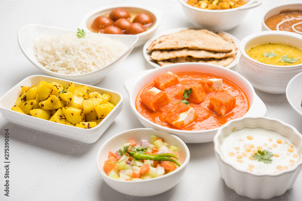 Assorted Indian food like paneer butter masala, dal, roti, rice, sabji, gulab jamun and bound raita served in bowls over moody background, selective focus Assorted Indian food like paneer butter masala, dal, roti, rice, sabji, gulab jamun and bound raita served in bowls over moody background, selective focus