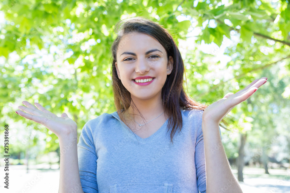 Excited pretty young lady throwing up hands in park. Beautiful woman wearing hoodie and looking at camera with green trees in background. Happiness and nature concept. Front view. Excited pretty young lady throwing up hands in park. Beautiful woman wearing hoodie and looking at camera with green trees in background. Happiness and nature concept. Front view.