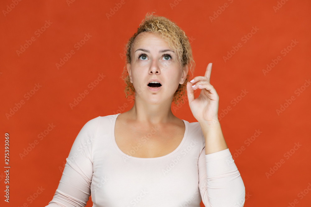 Fototapeta premium Photo portrait of a beautiful girl blonde woman with short curly hair on a red background talking and showing a lot of emotions. An experienced model shows hands. Beauty. Made in studio