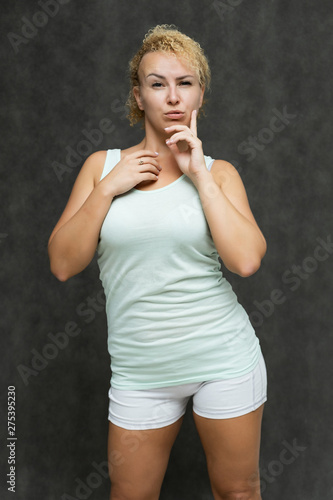 Photo portrait above the knee of a beautiful girl blonde woman with short curly hair on a gray background in bright linen is talking and showing a lot of emotions. An experienced model shows hands.