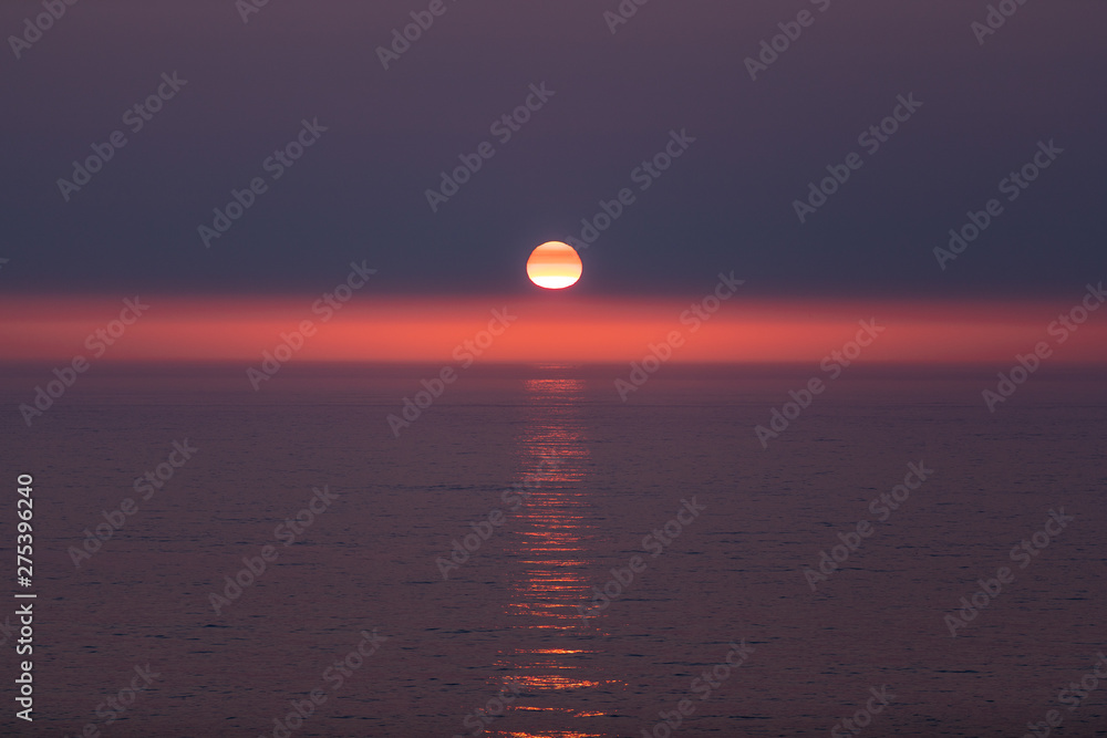 Sunset mirage. Sun  with red, orange and yellow stripes over it. Horizon highlighted in red with a perfect sun path on an ocean surface