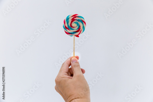Fun and celebration concept.hand holding big colorful lollipop candy on stick, isolated on white background minimalism style.