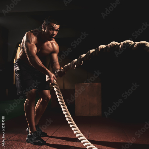 Muscular strong young man training with battle rope