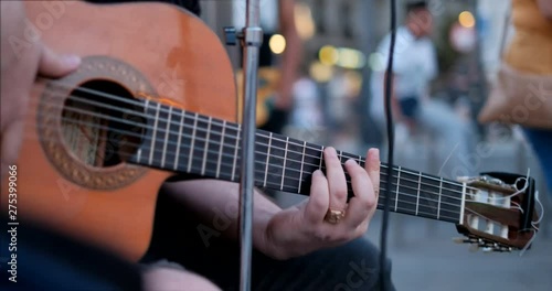 Young man playing guitar and singing song on sidewalk. Street artist with musical instrument in Madrid, Spain, Europe. Singer, music and arts. Close-up of strings and fingers