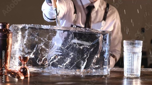 Foto bartender splits a block of ice to cool cocktails, barmen splitting huge clear ice block to two parts by using an ice pick and hammer