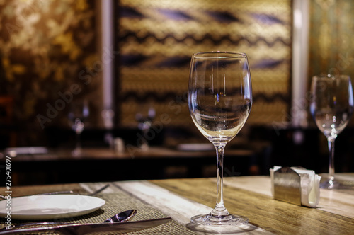 Empty clean wine glasses and tableware close up view on wooden table at exotic restaurant with persian carpet on the wall