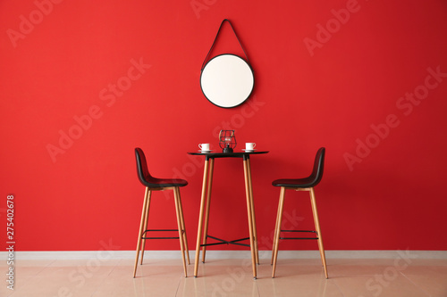 Table and chairs near color wall with mirror