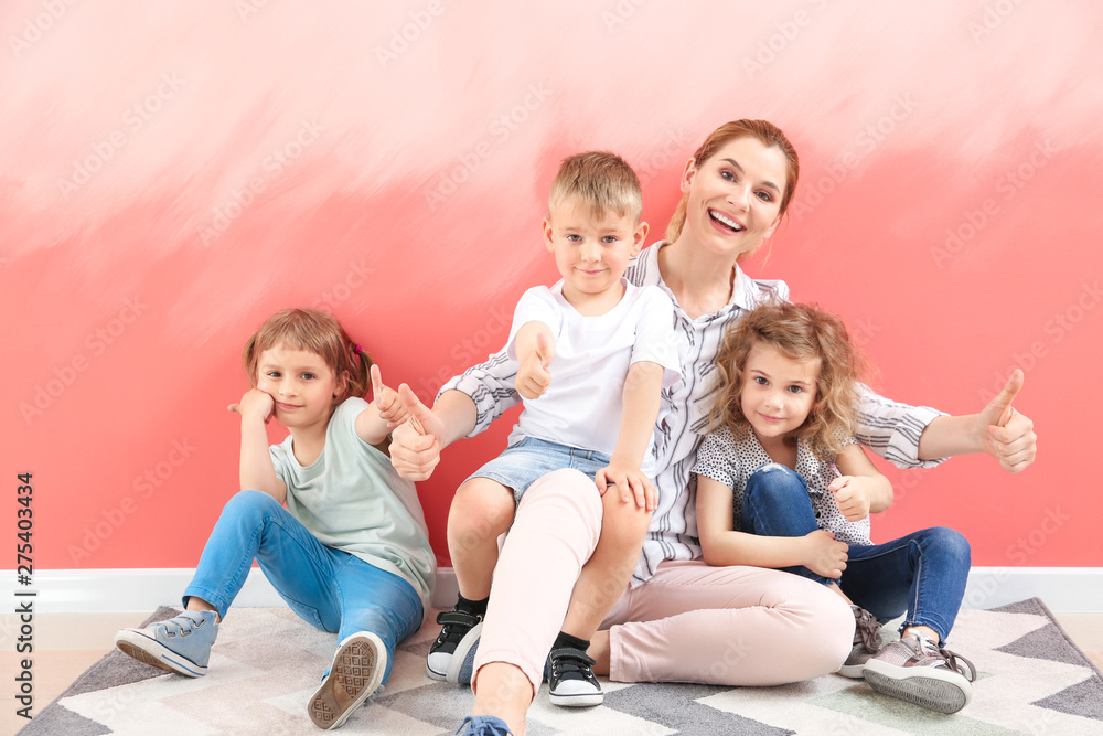 Cute little children with nursery teacher showing thumb-up gesture near color wall Cute little children with nursery teacher showing thumb-up gesture near color wall