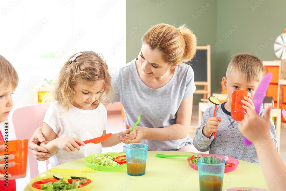 Fototapeta premium Nursery teacher with cute little children during lunch in kindergarten