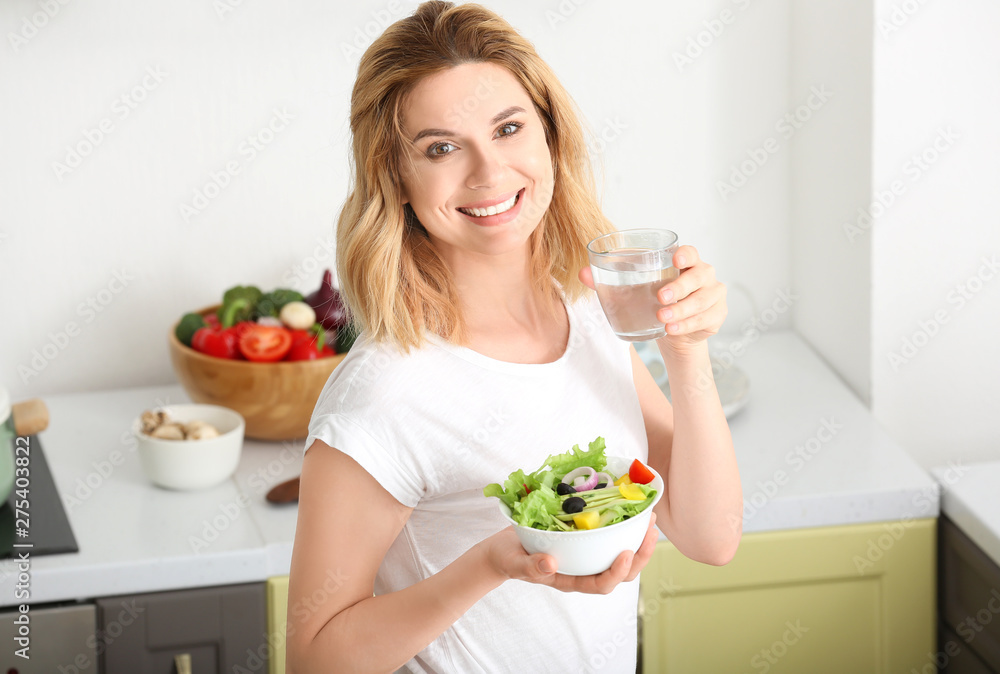 Woman with healthy vegetable salad and glass of water in kitchen Woman with healthy vegetable salad and glass of water in kitchen
