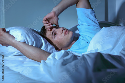 фотографія Young man suffering from insomnia while lying in bed at night